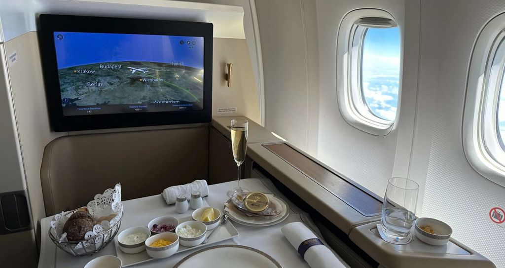 First-Class-Sitz mit Bildschirm, Champagner und gedecktem Tisch am Fenster